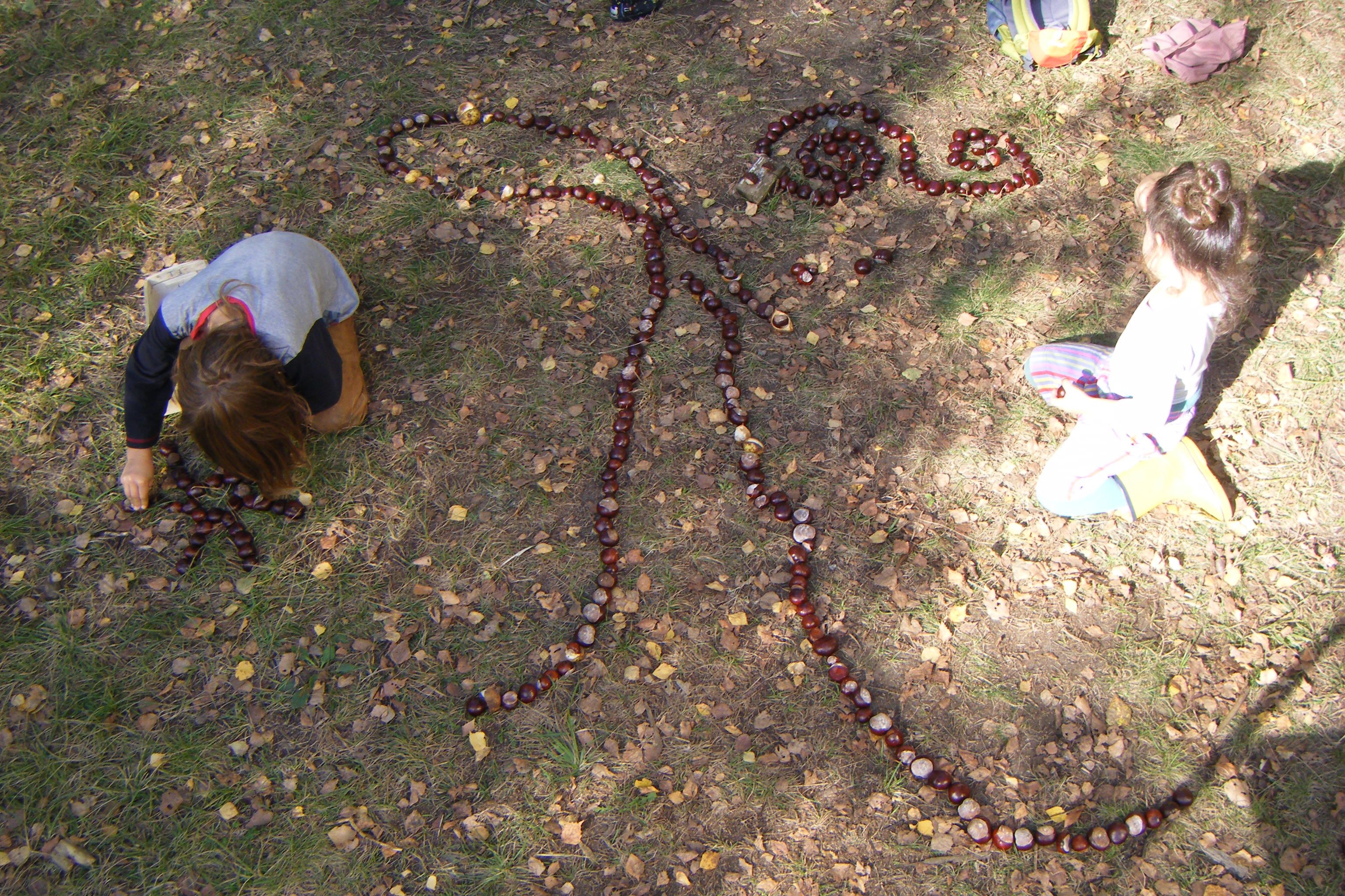 ein Kind legt ein weiters Muster aus kastanien auf den Waldboden