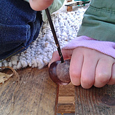 Kinderhände bohren mit einem Handbohrer ein Loch in eine Kastanie